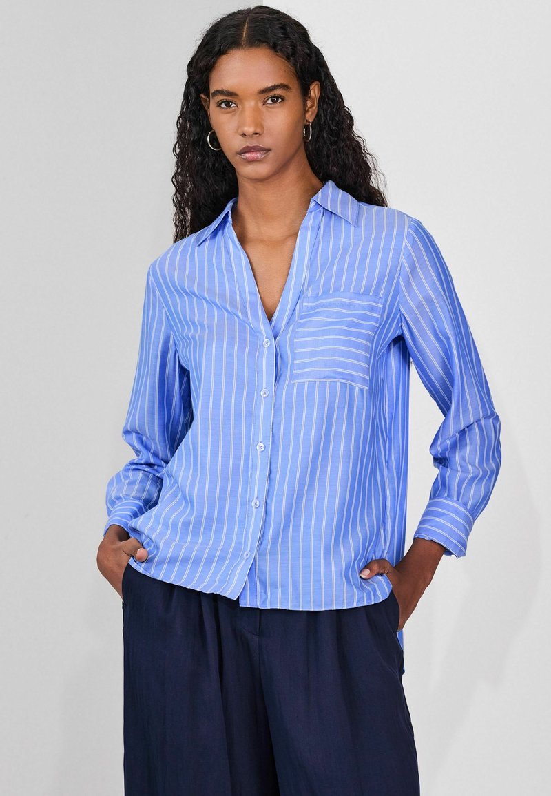 Light blue button-up shirt with vertical white stripes, features a collar, a single chest pocket, and long sleeves. Textured, breathable fabric.