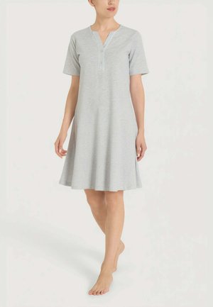 Donna in piedi a piedi nudi che indossa un vestito grigio chiaro al ginocchio, maniche corte e scollo con bottoni frontali.