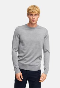 Maglione grigio a maniche lunghe in maglia con colletto a girocollo. Texture liscia, design aderente e polsini e orlo a coste. Indossato con pantaloni scuri.