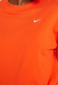 Orange bomullströja med rund hals, korta ärmar och en liten vit Nike-logotyp på vänster bröst. Slät textur.