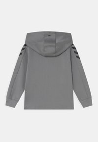 Grå hetsare med en slät textur, med svarta ränder på axlarna och en logotyp broderad på ryggen.