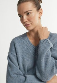 Jasnoniebieski sweter dziany z dekoltem w serek i przeskalowanymi rękawami, z prążkowanymi mankietami i teksturowanym wzorem na całej powierzchni.