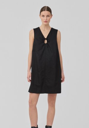 Vestido negro sin mangas con escote en V y una abertura en forma de llave con detalle de lazo. La tela parece suave con una silueta recta y relajada.