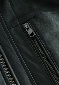 Zwarte leren jas met een diagonale rits en metalen hardware. Gladde textuur met zichtbare stiksels en ritszakken.