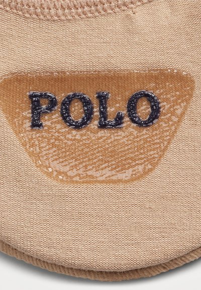 Šviesiai ruda audinio etiketė su tekstūruotu fonu ir blizgiu paviršiumi, kuriame tamsiai mėlynomis raidėmis išsiuvinėta žodis "POLO".