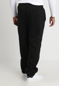 Black sweatpants made from soft fabric, featuring an elastic waistband and a single rear pocket. Accented with a vertical seam and cuffed hems.