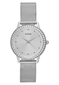 Montre argentée avec un bracelet en maille, cadran rond, lunette en cristal et un cadran minimaliste avec des marqueurs d'heure en forme de points et des aiguilles. Nom de la marque "Guess" affiché.