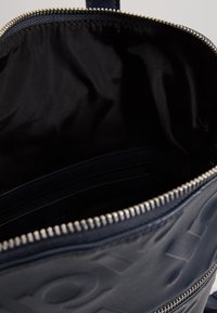 Sac en tissu bleu marine avec une texture lisse, doté d'une fermeture éclair argentée et d'un intérieur doublé. Comprend une poche intérieure pour les petits objets.