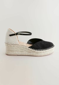 Sandalo con zeppa in suede nero, con tomaia tessile intrecciata bianca e nera, cinturino alla caviglia e piattaforma avvolta in juta. Suola in gomma piatta.
