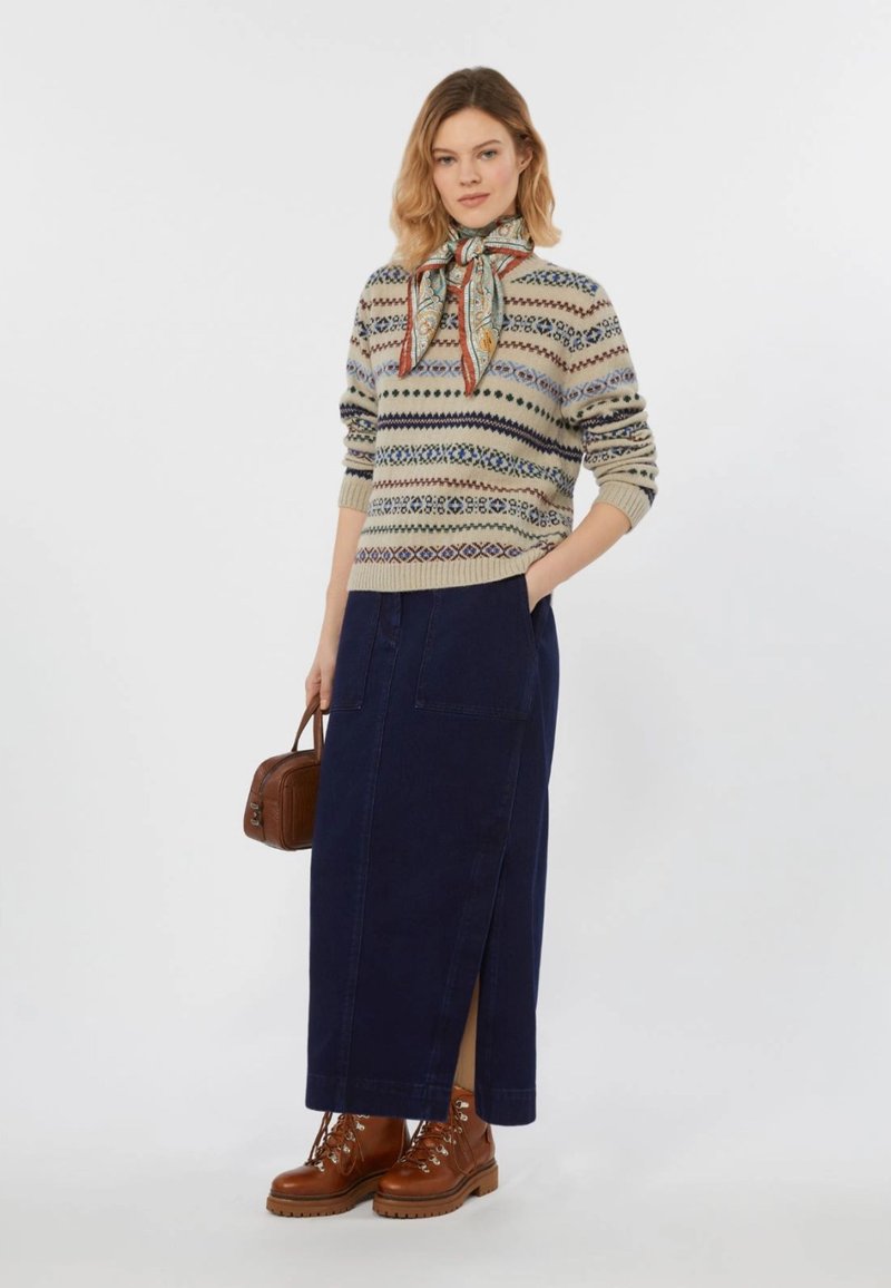 Maglione a maglia con design a fantasia e gonna maxiin denim blu con spacchi laterali. Stivali alla caviglia marroni e una piccola borsa marrone completano il look.