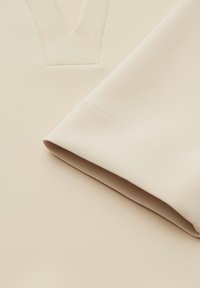 Top color crema con scollo a V, trama liscia e orlo delle maniche piegato con cuciture ordinate. Tessuto leggero e morbido.