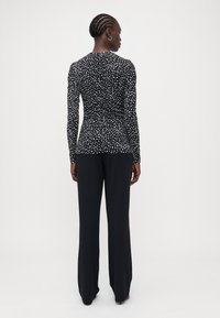 Haut à manches longues noir avec un motif abstrait blanc, design ajusté et tissu doux ; associé à un pantalon large noir.