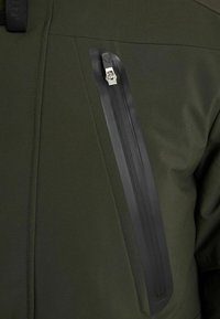 Ciemnozielona kurtka z diagonalnym wzorem; posiada wąską, matową czarną kieszeń na suwak na piersi, wykonaną z gładkiej, teksturowanej tkaniny.