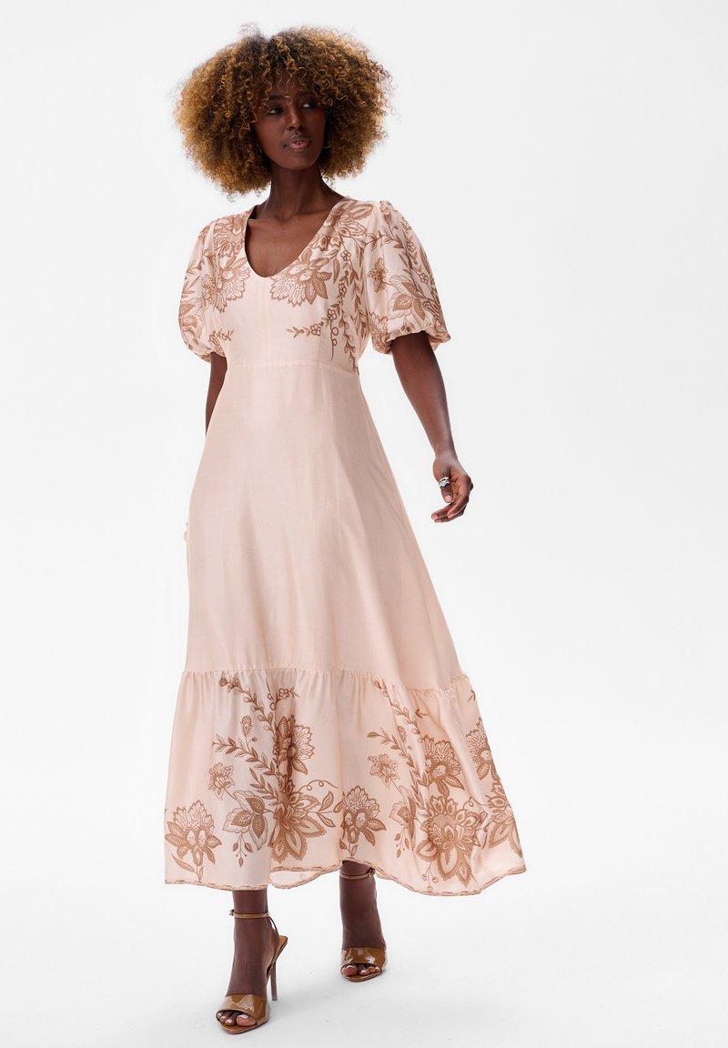 Maxi jurk van zacht perzikkleurig stof, met korte pofmouwen en bloemborduursel in brons. De zoom heeft een gerimpeld detail.