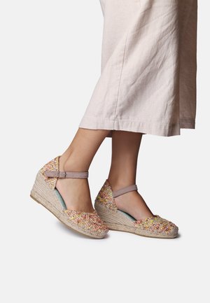 Nohy v pastelových viacfarebných tkaných klinových espadrilách s členkovými remienkami a svetlo ružových širokých nohaviciach.