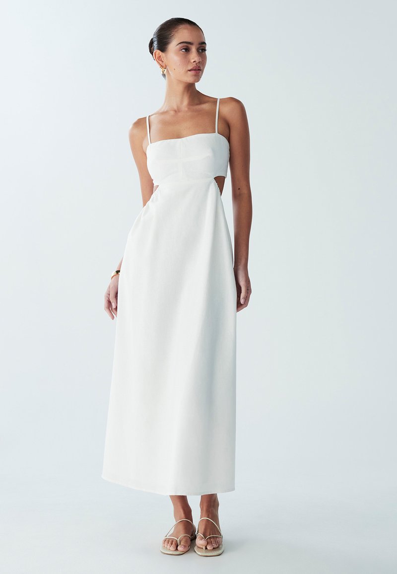 Vestido blanco de largo hasta el suelo que presenta un corpiño ajustado con tirantes finos y detalles recortados en la cintura. Tela suave y ligera con textura mínima.