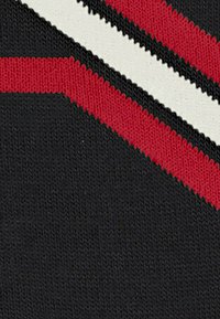 Tissu tricoté en noir avec des rayures diagonales rouges et blanches. Texture douce avec un léger éclat, présentant un contraste de couleurs audacieux et un design moderne.