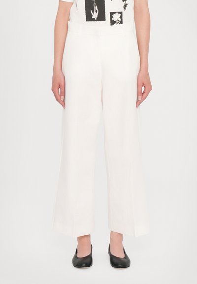 Pantalons larges blancs avec une texture lisse, dotés d'une taille haute et de lignes épurées, associés à des chaussures plates noires.