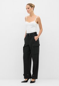 Zwarte cargobroek met zijzakken, gecombineerd met een witte aansluitende tanktop. Hoge hakken maken de look af en benadrukken het minimalistische ontwerp.