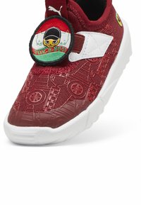 Chaussure en textile rouge avec un motif texturé, accents blancs et un patch circulaire représentant un personnage. Semelle en caoutchouc épaisse pour un bon maintien.