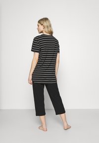 T-shirt a righe bianche e nere con maniche corte, abbinato a pantaloni neri a metà polpaccio; tessuto morbido, vestibilità rilassata e taglio dritto.