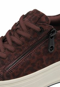 Baskets bordeaux avec une texture en daim, imprimé léopard, lacets plats, un accent de fermeture éclair noire et une semelle en caoutchouc blanche.