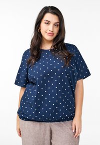 Top blu navy a maniche corte con pois bianchi, caratterizzato da un collo rotondo e un orlo elastico per una vestibilità ampia. Tessuto liscio e leggero.