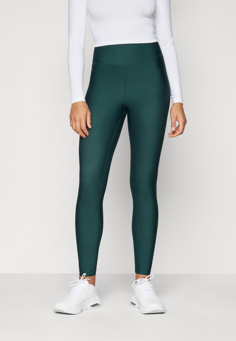 Leggings de cintura alta en tela verde oscura con una textura suave, combinados con zapatillas deportivas blancas. Diseño minimalista, sin patrones visibles.