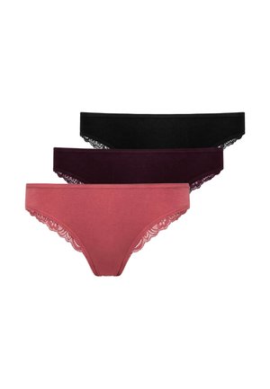 Frau trägt passenden rosafarbenen Spitzen-Bralette und einfarbige Unterhose und steht vor einem schlichten hellen Hintergrund.