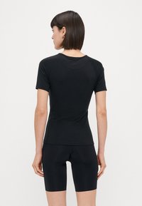 Zwarte fitted t-shirt met korte mouwen en ronde hals. Gemaakt van een glad materiaal, met raglanmouwen en minimale naden.