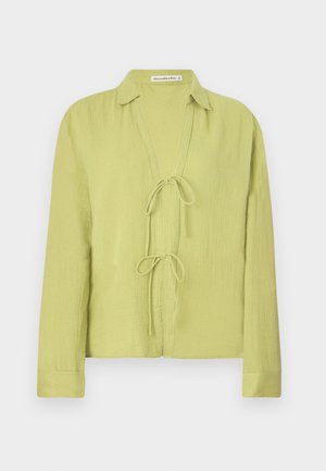 Chemise verte clair à manches longues en tissu froissé. Présente un devant sans boutons avec une fermeture à nouer et un col.