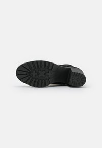 Sola di calzature nera con un pattern di grip testurizzato, caratterizzata da scanalature profonde e tasselli multidirezionali per trazione e stabilità.