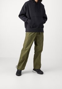 Sudadera con capucha negra y gran bolsillo frontal, combinada con pantalones cargo verde olivo, con dobladillos ajustables y zapatillas deportivas negras.