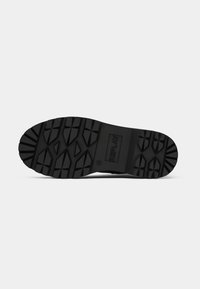 Black rubber shoe sole featuring a textured grip pattern with angular shapes and a central logo. Durable, designed for traction and stability.