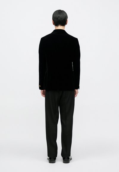 Μαύρο βελούδινο σακάκι με εφαρμοστή γραμμή, μονό πίσω άνοιγμα και διακοσμητικά χρυσά κουμπιά. Συνδυάζεται με μαύρο παντελόνι με εφαρμοστή γραμμή και παπούτσια.