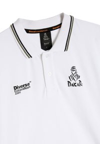 Biała koszulka polo z czarnym i oliwkowozielonym paskiem przy kołnierzy, z dwoma guzikami oraz nadrukowanymi czarnymi logo "Dakar" i "DiverseExtremeTeam.com".