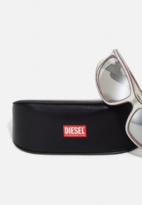 Čierny kožený puzdro na slnečné okuliare s červeným logom "DIESEL". Slnečné okuliare so strieborným nádychom majú odvážny rám s zaoblenými hranami a zložitým detailom.