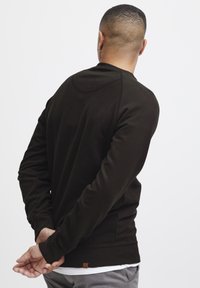 Sweatshirt vert foncé en matériau doux avec de longues manches, des poignets côtelés et une petite étiquette en cuir à l'ourlet. Vue arrière montrée.