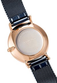 Montre ronde avec un fond en acier inoxydable, un boîtier doré, un bracelet en mailles noires et une couronne poussoir ; présente des détails de marque et de mouvement gravés.