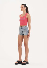 Top corto rosa con un gráfico multicolor, combinado con unos pantalones cortos de denim azul claro con acentos bordados, y sandalias de plataforma negras.