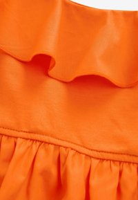 Oranje stof met een gerimpelde bovenrand en een geplooid textuur aan de onderkant, gekenmerkt door een gladde, lichte materialen en een consistente kleur.