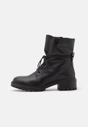 Bottes noires en cuir, à la cheville, avec un bout arrondi, un laçage avant et un petit talon carré. Semelle texturée avec un motif de crampons robuste.