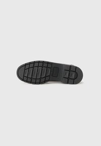 Suola di scarpa in gomma nera con battistrada a motivo, caratterizzata da scanalature e rilievi per una migliore aderenza. Design resistente con una finitura testurizzata.