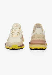 Zapatillas deportivas beige con una mezcla de materiales texturizados, que incluyen ante y textil, con una suela gruesa amarilla y sutiles acentos marrones.