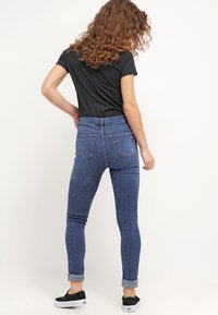Jeans de denim ajustados en azul oscuro, con una cintura alta, dos bolsillos traseros y puños remangados. Combinados con una camiseta negra y zapatos negros.