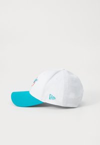 Hvitt caps med turkise visir, som har en delfinlogo brodert i oransje og aqua. Inkluderer en liten blå logo på siden.