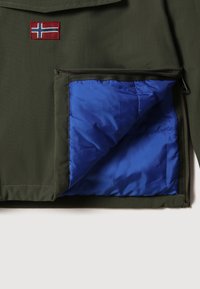 Veste verte avec une poche partiellement dézippée révélant une doublure matelassée bleu vif et un petit écusson avec le drapeau de la Norvège au-dessus de la poche.