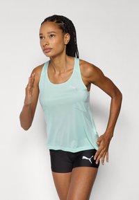 Sporttanktop in licht muntgroen met een gaasstructuur, voorzien van een subtiele logo op de borst; gecombineerd met zwarte shorts versierd met een logo.