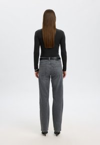 Črn dolg rokav z oprijetim krojem, kombiniran z visokim pasom sivih kavbojk. Kavbojke imajo zadnje žepe in ravne hlačnice.