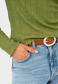 Lichtgroene geribbelde trui met gegolfde manchetten, gecombineerd met blauwe jeans en een bruine riem met een ronde, zilveren gesp.